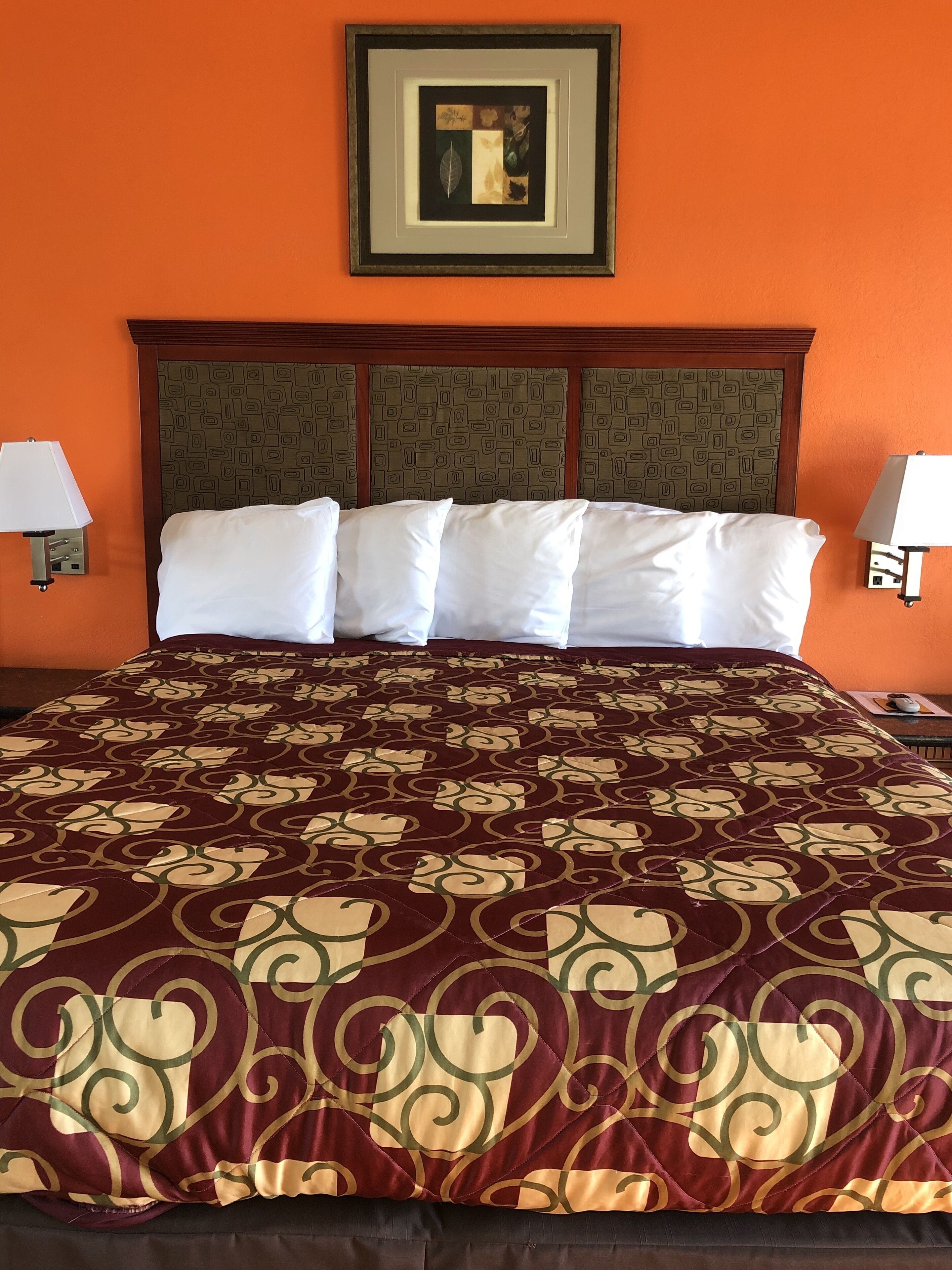 A hotel room with a large bed, a patterned bedspread, a framed artwork above the bed, and two bedside lamps.
