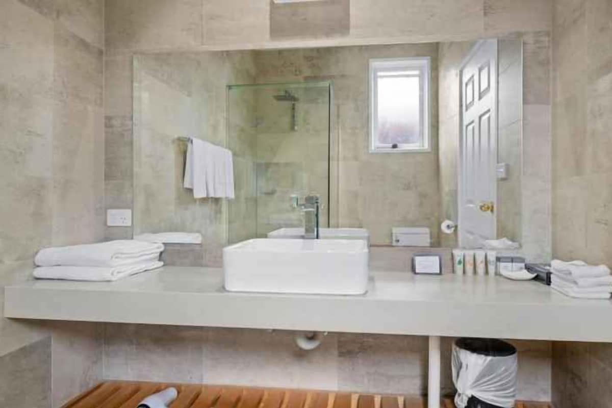 A modern bathroom with a large mirror, a white sink, and a towel rack.