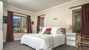 A bedroom with a large bed, two bedside tables, a nightstand, and a view of a mountainous landscape through the windows. - Wilkes Way Villa (Picton)