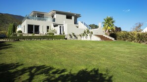 A modern two-story house with a large front lawn, a staircase leading to the entrance, and a clear blue sky. - Wilkes Way Villa (Picton)