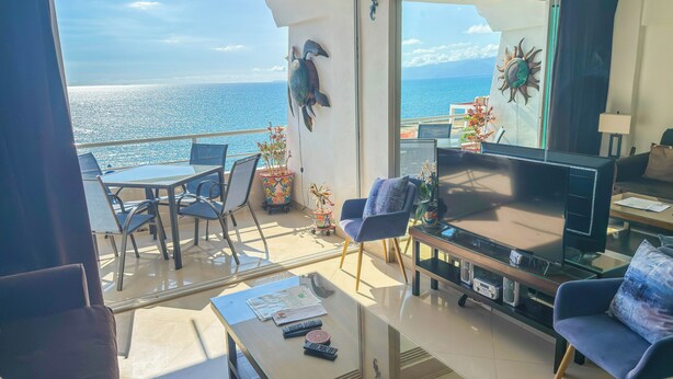 Un balcon avec vue sur la mer, aménagé avec une table, des chaises et un téléviseur.