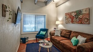 A living room with a brown sofa, a blue armchair, a TV mounted on the wall, and a window with blinds. - #5: Walk to Old Town Plaza, King & Queen beds, 2 TV's (Albuquerque)
