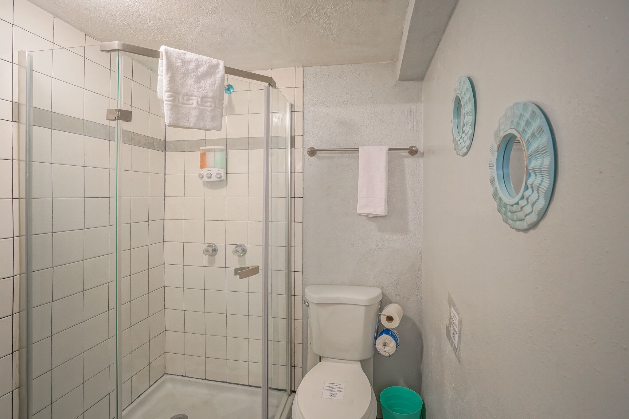 Ett badrum med en dusch som är avskärmad med glasväggar, en toalett och två handdukshängare som är monterade på väggen.