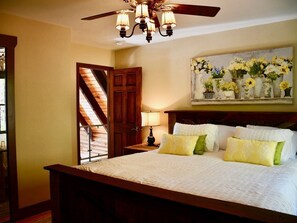 A bedroom with a large bed, a ceiling fan, a wooden door, and a painting of flowers on the wall. - Cabin, hot tub, High Speed Internet, fire pit, resort, hiking, boating,spa,golf (Lake Lure)