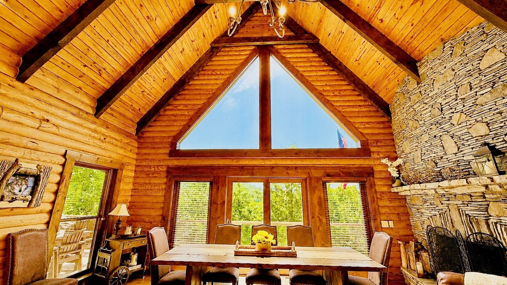 A log cabin interior with a dining table, chairs, a fireplace, and a large window.