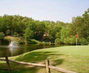 A golf course with a pond, a wooden fence, and a red flag marking the hole. - Cabin, hot tub, High Speed Internet, fire pit, resort, hiking, boating,spa,golf (Lake Lure)