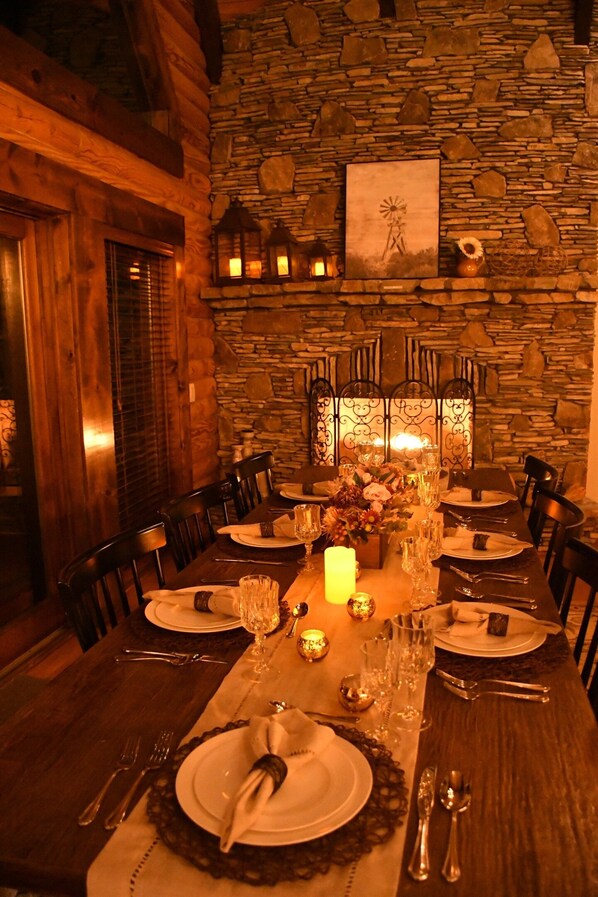 Enjoy meals in this cozy dining area with a long table, centerpiece, and fireplace.