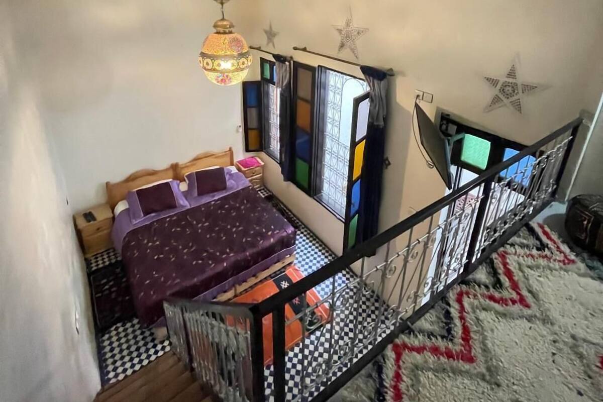 A compact room with a bed, a small table, and a hanging lamp. There is a window with a view of the outside.
