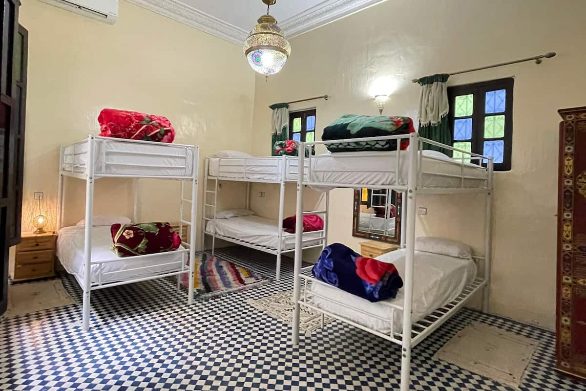 A room with bunk beds, a patterned floor, a hanging light fixture, and a window with curtains.