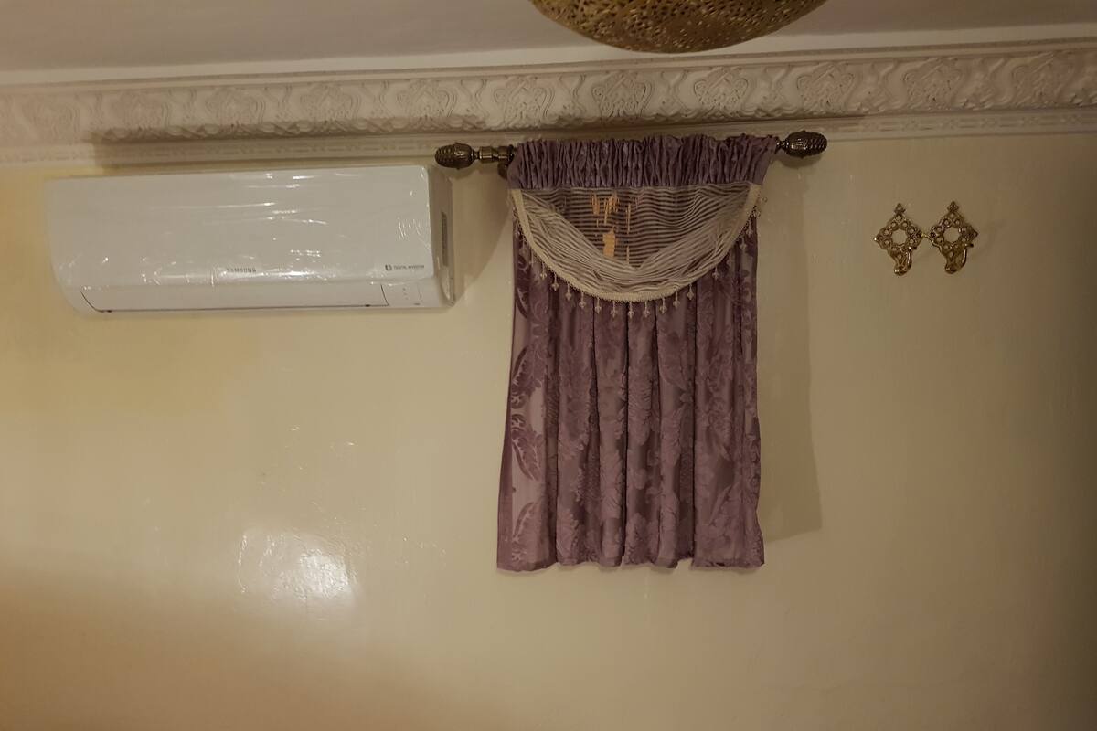 A room with a wall-mounted air conditioner, a decorative curtain, and a wall-mounted light fixture.