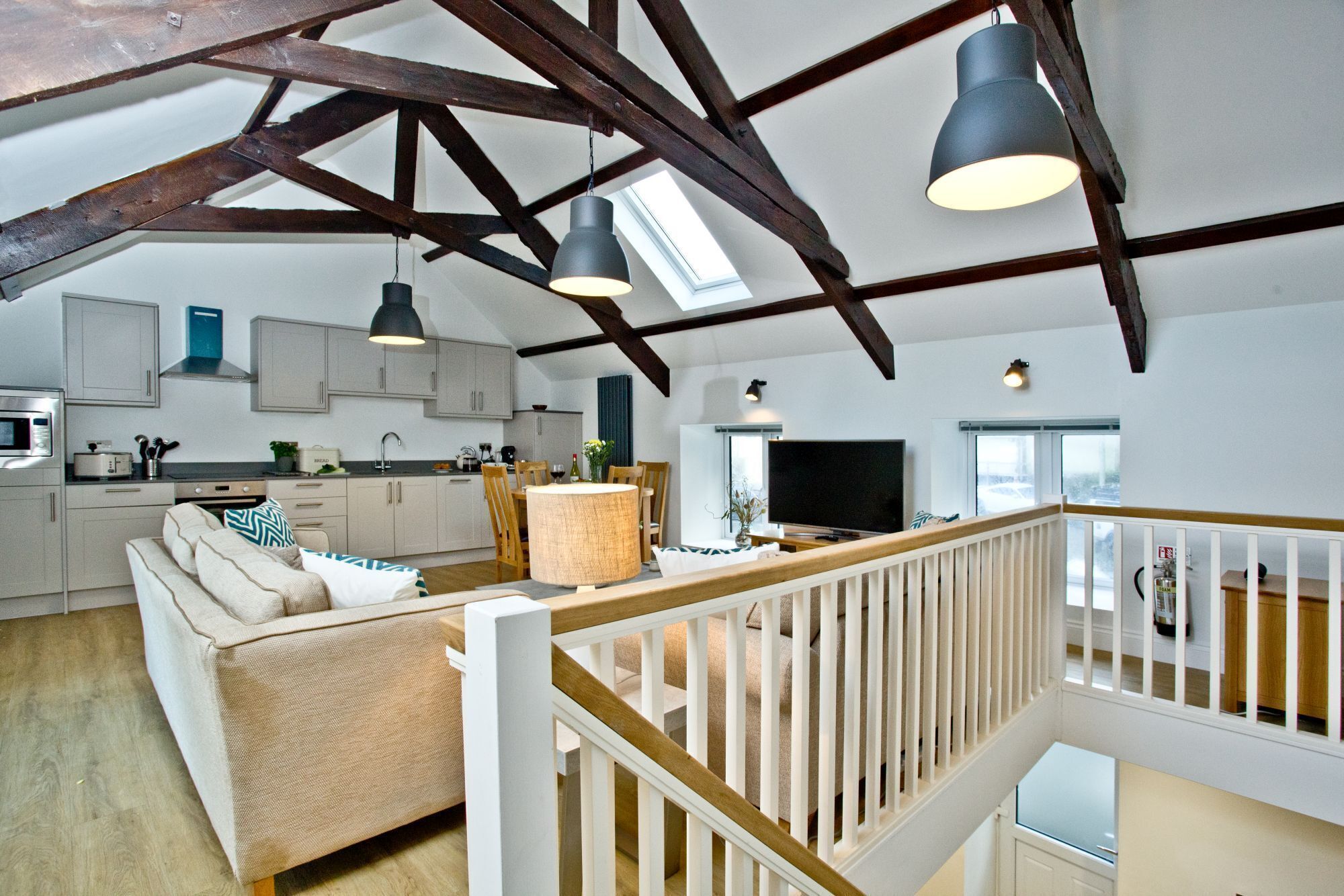 A spacious loft with exposed wooden beams, a kitchen with modern appliances, a dining area, and a living room with a TV.
