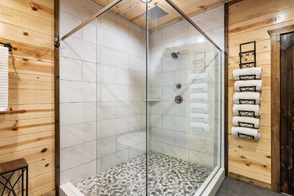 Eine begehbare Dusche mit Glaswand, gefliestem Boden, Holzvertäfelung und einem Handtuchhalter mit Handtüchern.