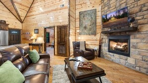 A cozy log cabin interior with a leather sofa, a stone fireplace, and a television mounted above it. - Easy Living -Mountain Setting w/ Pool Table & Private Hot Tub🎱🌲♨️ (Broken Bow)