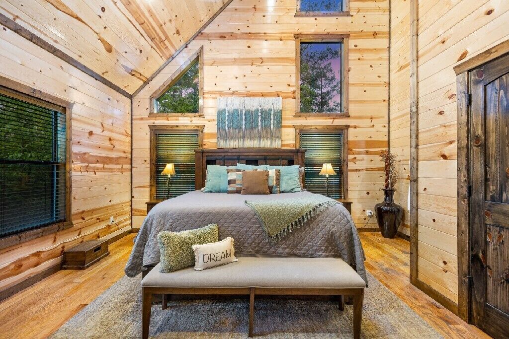 A cozy bedroom with a large bed, a bench, and a window with blinds.