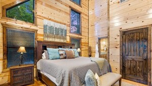 A wooden cabin bedroom with a large bed, a bench, and a wooden door. - Easy Living -Mountain Setting w/ Pool Table & Private Hot Tub🎱🌲♨️ (Broken Bow)