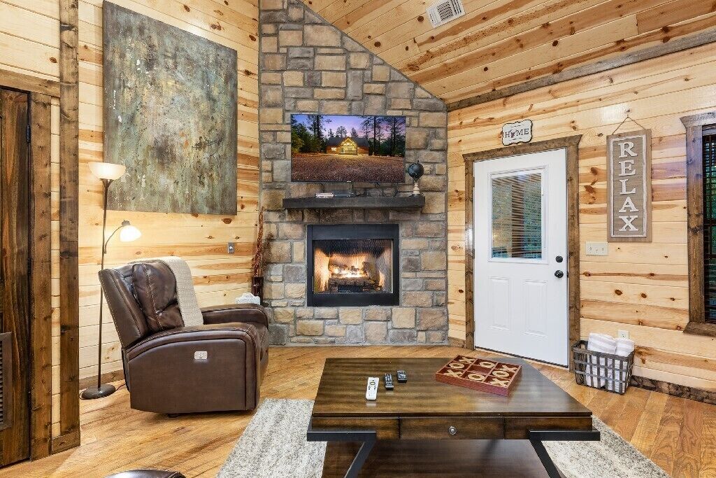 L'intérieur d'un chalet chaleureux, avec une cheminée en pierre, un fauteuil inclinable en cuir, une table basse et un panneau indiquant « RELAX » accroché au mur.