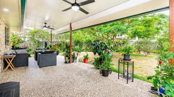An outdoor patio with a ceiling fan, seating area, and potted plants.