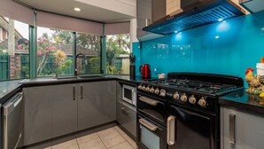 A modern kitchen with a gas stove, oven, and a view of a garden through large windows. - Delightful Duplex on Rose (BONGAREE)