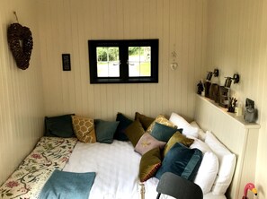Ein gemütliches Schlafzimmer mit einem Bett, Kissen, einem Fenster und einer Ablage mit Dekoration.