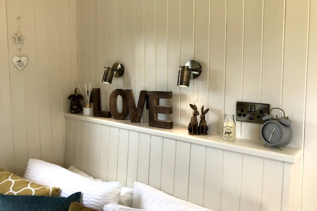 A bedroom with a bed, a shelf with decorative items, and a wall-mounted light fixture.