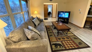 Ein Wohnzimmer mit einer Couch, Couchtisch, Fernseher und einem Teppich mit Bärenmuster.