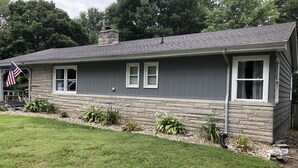 A two-story house with a stone foundation, a gray exterior, and a small front porch with an American flag. - CHARMING NEIGHBORHOOD IN PURDUE'S BACKYARD (West Lafayette)