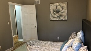A bedroom with a floral-patterned bedspread, a door leading to another room, and a large floral artwork on the wall. - CHARMING NEIGHBORHOOD IN PURDUE'S BACKYARD (West Lafayette)