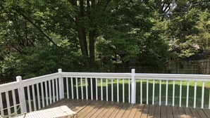 A wooden deck with a white railing, a metal table, and a grassy yard in the background. - CHARMING NEIGHBORHOOD IN PURDUE'S BACKYARD (West Lafayette)