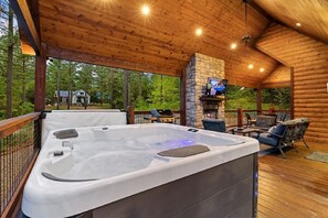 A hot tub with a stone fireplace, outdoor seating, and a TV on a stone wall. - Hard 8 - Relax and have fun with first-class amenities, a hot tub & game room! (Broken Bow)