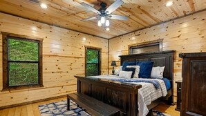 Quarto com painéis de madeira, uma cama, um banco e duas janelas.