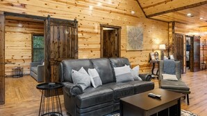 Interior de uma cabana de troncos com um sofá de couro, uma mesa de centro e uma mesa lateral.