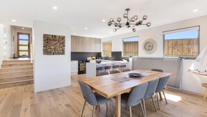 A modern kitchen with wooden cabinets, a central island, and a dining area with a wooden table and grey chairs.