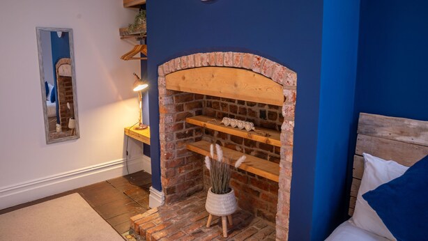 A room with a brick fireplace, a clock on the wall, and shelves with decorative items.