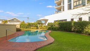 A swimming pool with a brick border, surrounded by a well-maintained lawn and a hedge. - Beach Pines 5 - Fully Renovated North Kirra Beachfront - Min. 3 Night Stays (Bilinga)