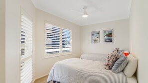 Una camera da letto con un letto, due finestre con persiane, un ventilatore a soffitto e due quadri appesi al muro.