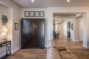 A modern living room with a large dark-colored refrigerator, a beige sofa, and a dining area with a table and chairs. - Epic Escape (St. George)