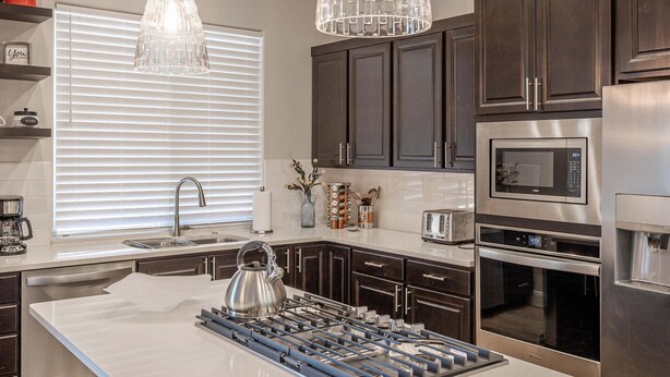 A modern kitchen with stainless steel appliances, dark wood cabinets, and pendant lighting.