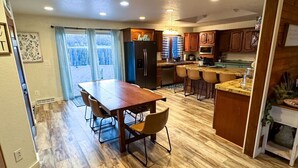 A spacious kitchen with wooden cabinets, a central island, and a dining area with a large table and chairs. - Theater Room | Hot Tub | Arcades | Great Location! (Spearfish)