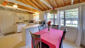 A kitchen with white cabinets, a wooden ceiling, a dining table with a red tablecloth, and a window with curtains. - Rustic Retreat Across from Lake; Family Friendly! (Union)