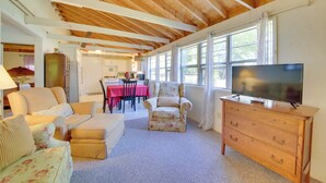 A living room with a wooden ceiling, a television on a dresser, and a dining area in the background. - Rustic Retreat Across from Lake; Family Friendly! (Union)