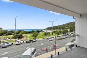 A view from a balcony overlooking a busy street with cars and pedestrians, a clear sky, and a hilly landscape in the distance. - Joy Apartment 2 (Lorne)