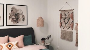 Ett sovrum med en säng, kuddar, en väggdekoration och en hängande lampa.