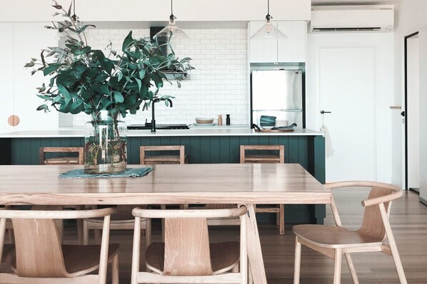 A modern kitchen with a central island, wooden chairs, and a potted plant. - Joy Apartment 2 (Lorne)