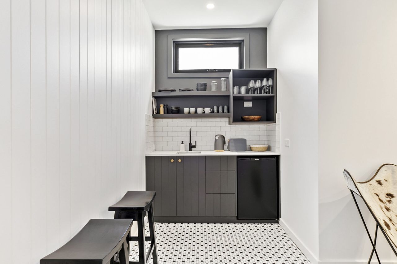 A compact kitchen with a built-in window, white tiled backsplash, dark cabinetry, and a small dining area with a bench.
