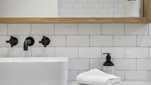 Et badeværelse med en hvid vask, sorte armaturer, et hvidt håndklæde og en flaske Glow Lab sæbe.