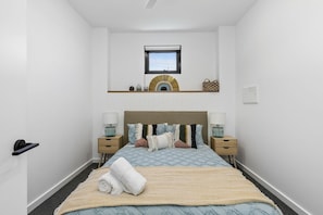 Ein Schlafzimmer mit einem Bett, Nachttischen, einem Fenster und einem an der Wand befestigten Regal.