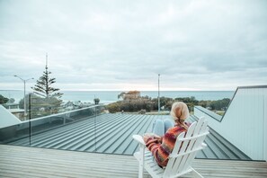 A person sitting on a white chair on a rooftop terrace overlooking a body of water. - Joy Apartment 3 (Lorne)