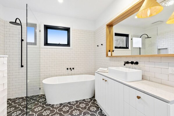 A modern bathroom with a freestanding bathtub, a large mirror, and a window.