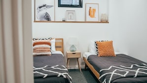Un dormitorio con dos camas, una mesita de noche, un ventanal y decoración en la pared.