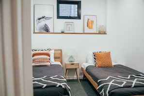 A bedroom with two beds, a nightstand, a window, and wall art.